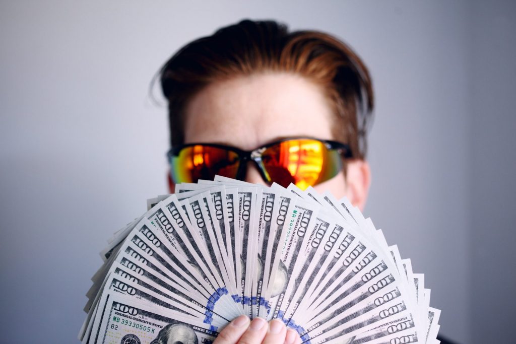 a man in yelow glasses holding a stack of a hundred dollar notes
