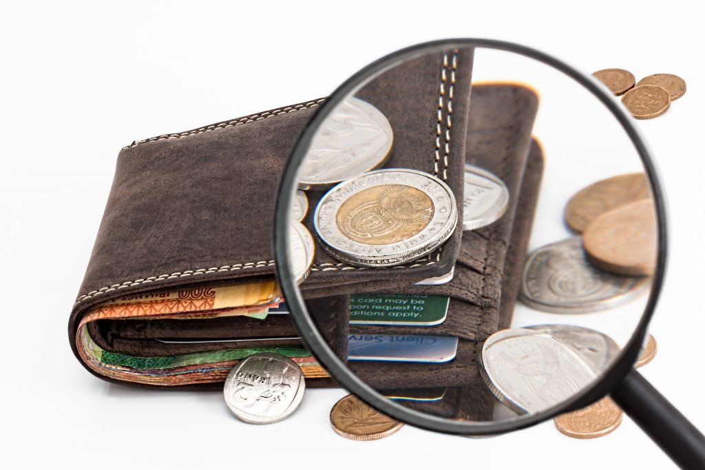a wallet with coins and notes with a magnifying glass on top of them
