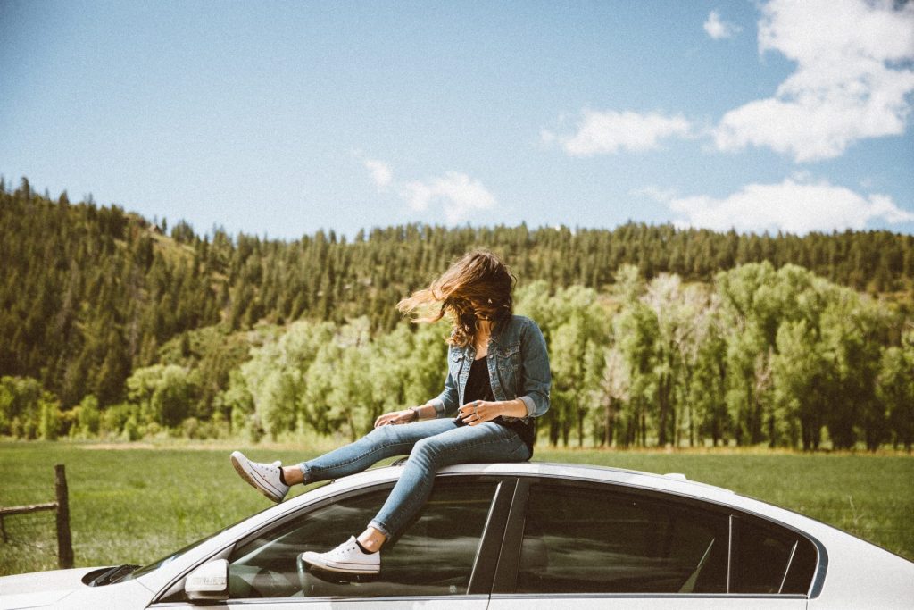 a girl sitting on the top of a car with woods background