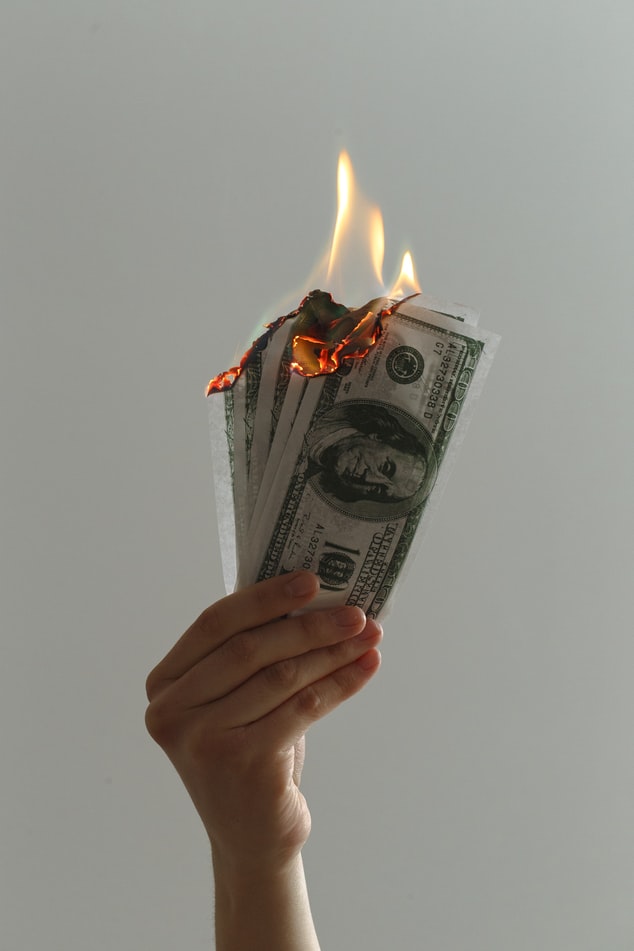 a hand holding dollar notes in flames