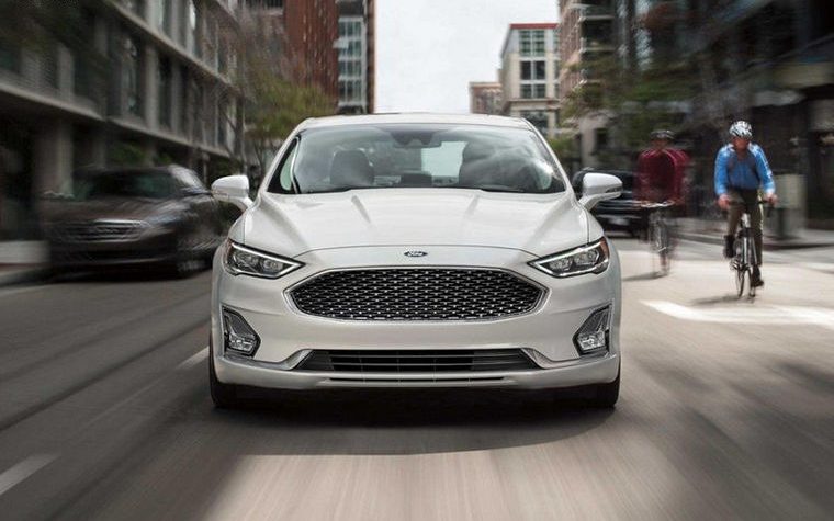 white ford fusion in the motion with a cyclists on the side